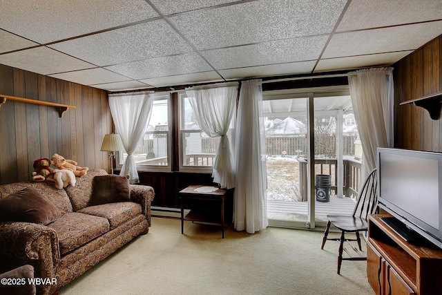 living room with light carpet, wooden walls, baseboard heating, and a drop ceiling