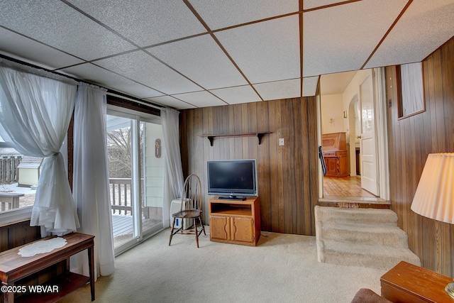 carpeted living area featuring a paneled ceiling, wood walls, arched walkways, and stairs