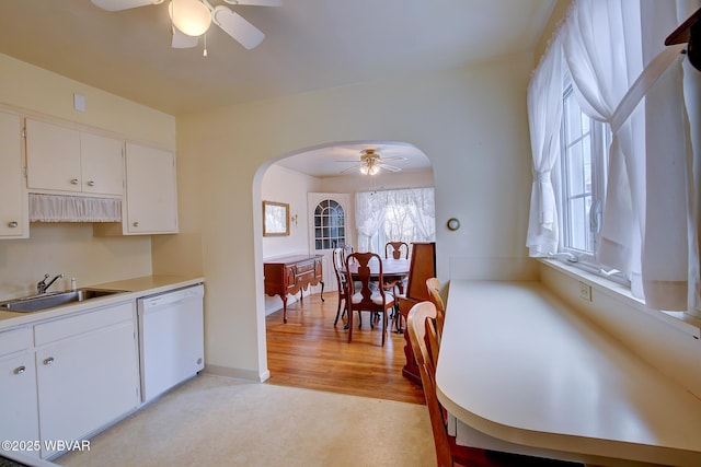 kitchen featuring arched walkways, white dishwasher, light countertops, white cabinetry, and a sink