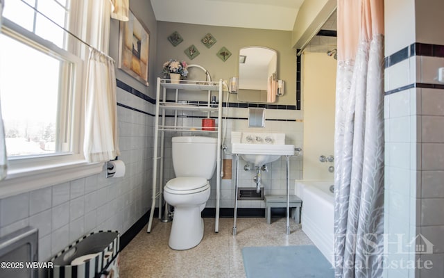 bathroom featuring toilet, wainscoting, shower / tub combo, tile walls, and speckled floor