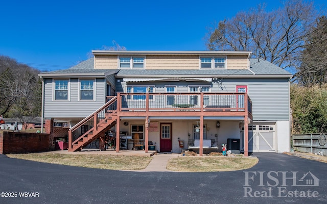 view of front of home featuring stairway, fence, an attached garage, a deck, and aphalt driveway