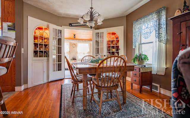 dining space with visible vents, light wood-style flooring, baseboards, and an inviting chandelier