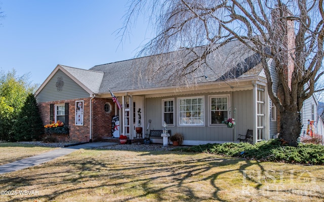 view of front of home with a front lawn, brick siding, and roof with shingles