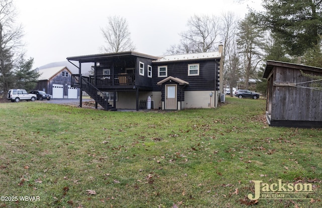 back of house featuring a lawn, a wooden deck, an outbuilding, and a garage