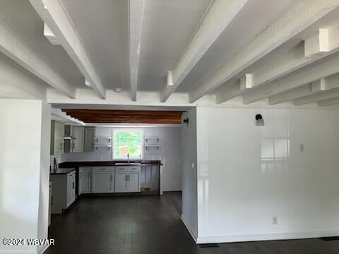 kitchen with dark countertops, dark wood-type flooring, a sink, beamed ceiling, and baseboards