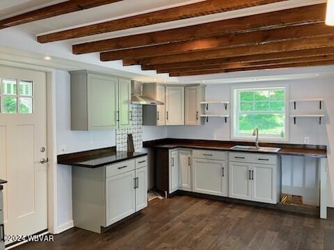 kitchen with a sink, wall chimney range hood, dark wood-style floors, open shelves, and beamed ceiling