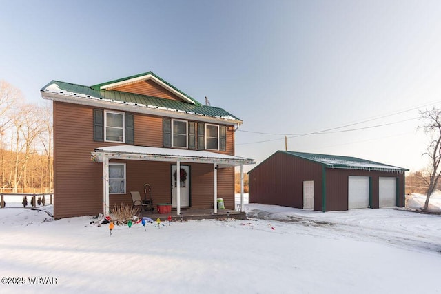 snow covered property with a garage, an outdoor structure, and covered porch