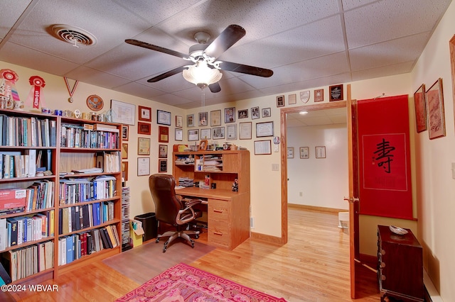 home office with a drop ceiling, light hardwood / wood-style flooring, and ceiling fan