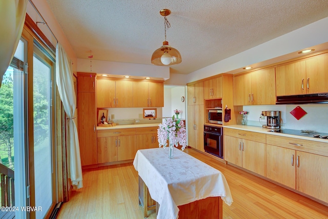 kitchen with black oven, cooktop, light wood-type flooring, and decorative light fixtures