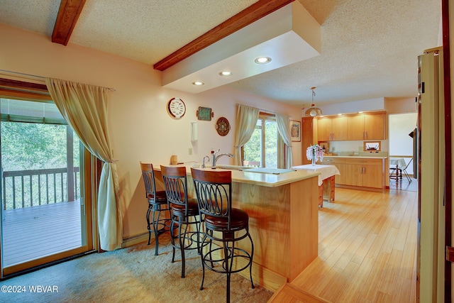 kitchen featuring kitchen peninsula, beam ceiling, a breakfast bar, and light hardwood / wood-style floors