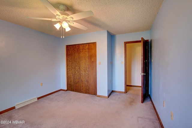 unfurnished bedroom featuring ceiling fan, light colored carpet, a textured ceiling, and a closet