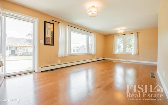 unfurnished room featuring baseboard heating, plenty of natural light, and light hardwood / wood-style flooring