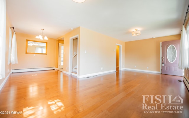 spare room featuring light hardwood / wood-style floors, an inviting chandelier, plenty of natural light, and a baseboard heating unit