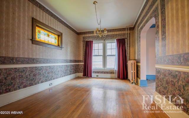 empty room with radiator, an inviting chandelier, wood-type flooring, and ornamental molding