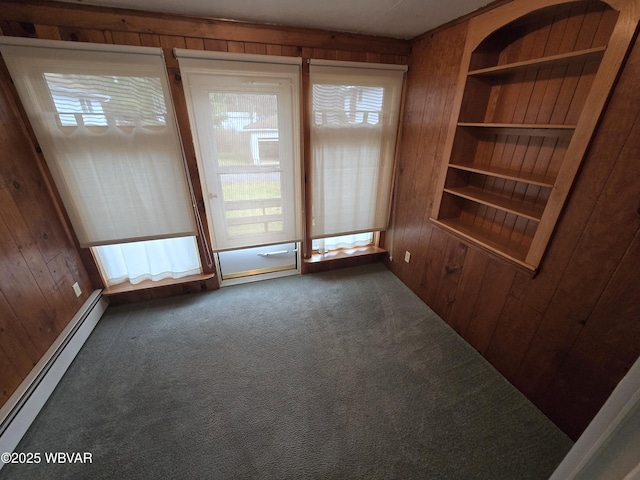 carpeted empty room with a baseboard radiator, built in features, and wood walls