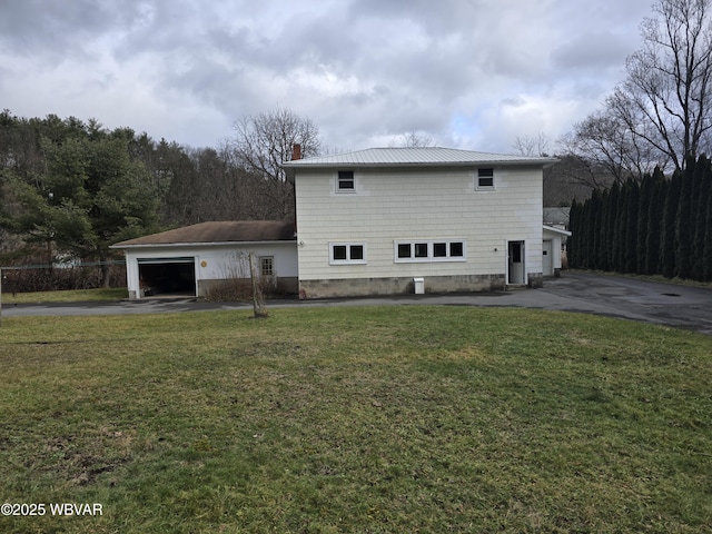 rear view of property with a chimney, driveway, a lawn, and an attached garage