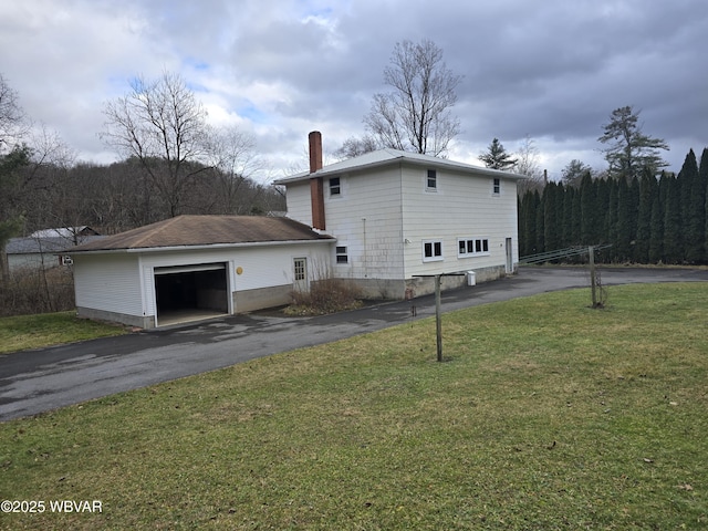 back of property featuring driveway, a garage, a chimney, and a yard