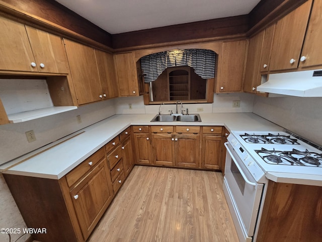 kitchen with under cabinet range hood, a sink, white range with gas cooktop, light countertops, and brown cabinets