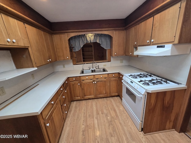 kitchen featuring light wood finished floors, white range with gas cooktop, light countertops, under cabinet range hood, and a sink