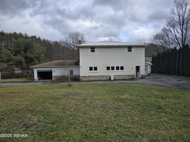 back of property featuring a yard, driveway, a chimney, and a garage