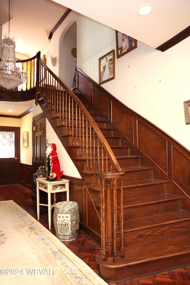 stairs with parquet flooring, an inviting chandelier, and crown molding