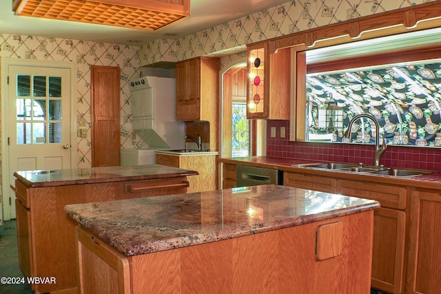 kitchen featuring decorative backsplash, stacked washing maching and dryer, dark stone counters, sink, and a kitchen island