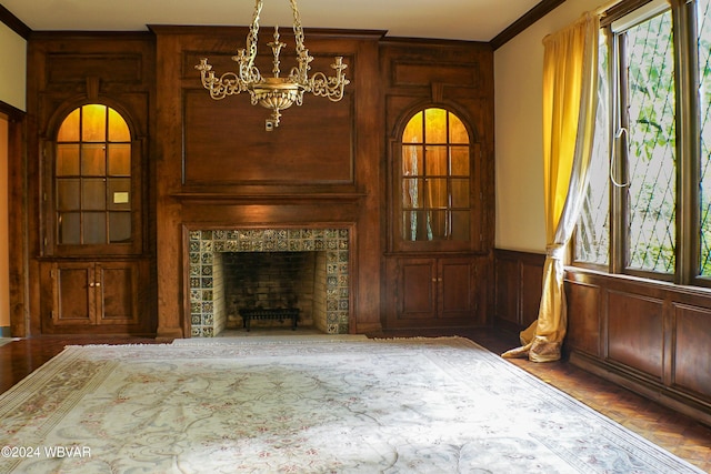 unfurnished living room with a chandelier, hardwood / wood-style flooring, ornamental molding, and a tiled fireplace