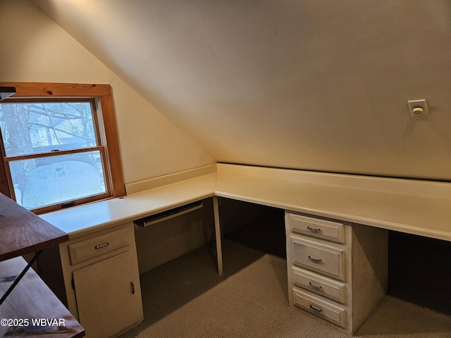 unfurnished office with lofted ceiling, light colored carpet, and built in desk