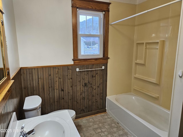 full bathroom featuring wooden walls, sink, bathtub / shower combination, and toilet