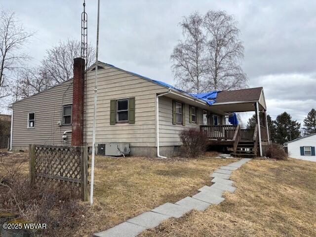 view of side of property with crawl space, a chimney, a deck, and a lawn