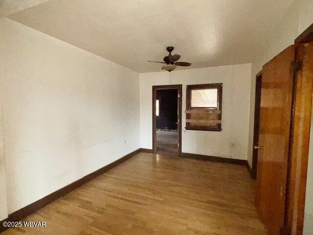 unfurnished room with wood finished floors, a ceiling fan, and baseboards