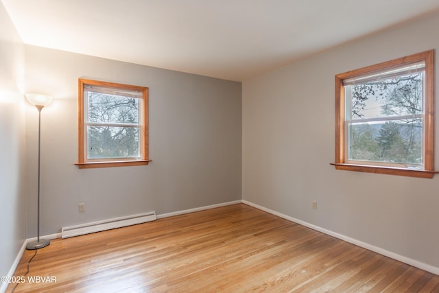 unfurnished room with a baseboard heating unit, a wealth of natural light, and light hardwood / wood-style flooring