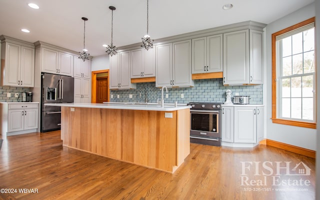 kitchen featuring decorative backsplash, appliances with stainless steel finishes, light wood-type flooring, pendant lighting, and an island with sink