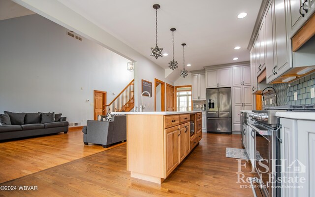 kitchen with pendant lighting, high quality appliances, a kitchen island with sink, and light hardwood / wood-style flooring