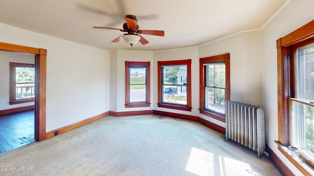 empty room featuring carpet flooring, radiator, crown molding, and ceiling fan