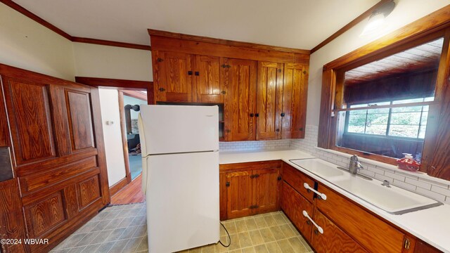 kitchen featuring decorative backsplash, white fridge, crown molding, and sink