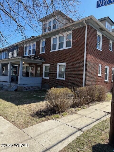 view of side of home featuring brick siding, a lawn, and covered porch