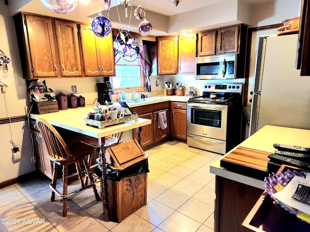 kitchen with light tile patterned floors, stainless steel appliances, a sink, light countertops, and brown cabinetry