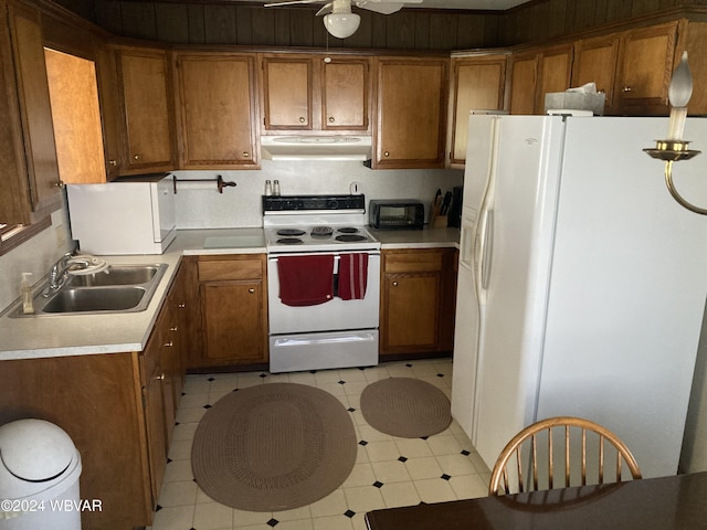 kitchen featuring white appliances, brown cabinetry, light floors, under cabinet range hood, and a sink