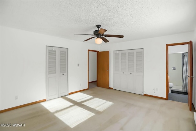 unfurnished bedroom featuring ensuite bathroom, ceiling fan, light carpet, and multiple closets