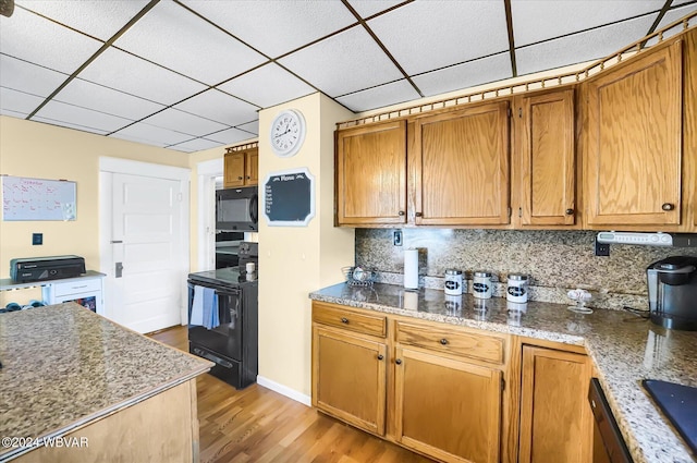 kitchen with light stone countertops, tasteful backsplash, light hardwood / wood-style floors, a paneled ceiling, and black appliances