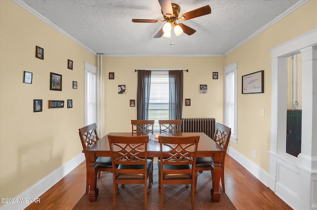 dining area featuring radiator heating unit, ceiling fan, ornamental molding, a textured ceiling, and wood-type flooring