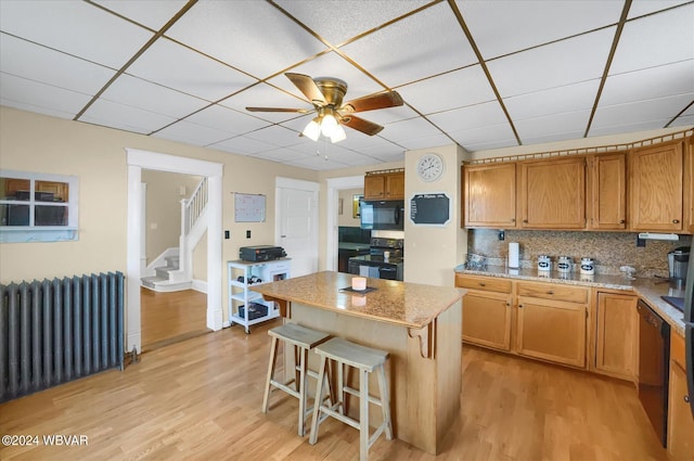 kitchen featuring radiator heating unit, a center island, tasteful backsplash, a breakfast bar, and black appliances