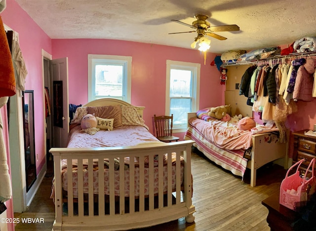 bedroom with a textured ceiling, ceiling fan, hardwood / wood-style floors, and multiple windows