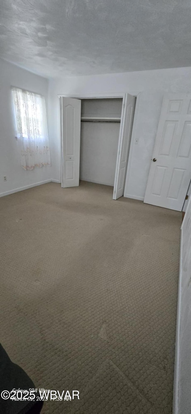 unfurnished bedroom featuring a closet, light colored carpet, a textured ceiling, and baseboards