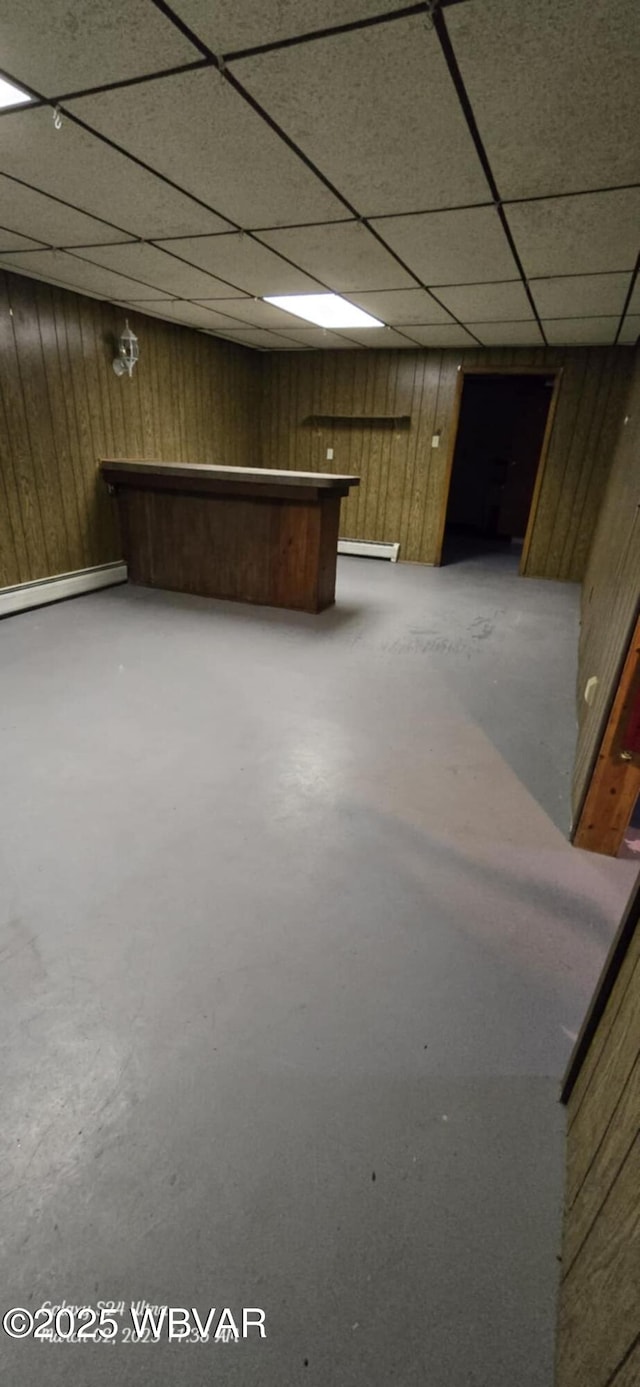 finished basement featuring a drop ceiling, wooden walls, and a baseboard heating unit