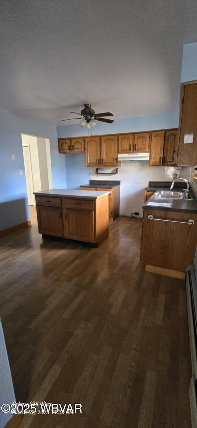 kitchen with a textured ceiling, dark wood-type flooring, brown cabinetry, and a sink