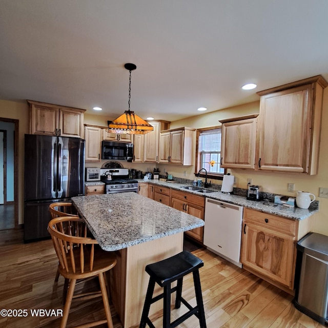 kitchen featuring light wood finished floors, light brown cabinetry, a breakfast bar, black appliances, and a sink