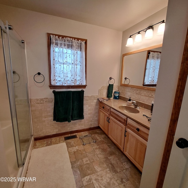 bathroom featuring visible vents, a stall shower, stone finish floor, wainscoting, and vanity