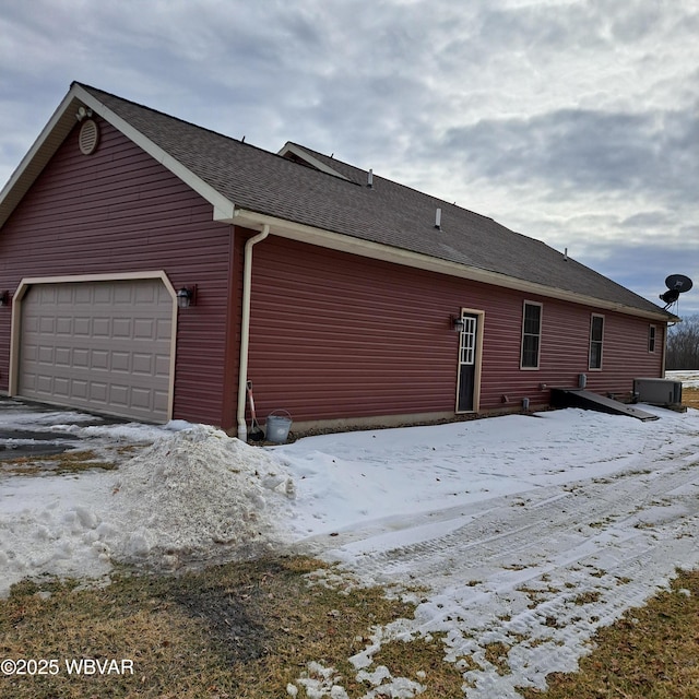 snow covered back of property with a garage and roof with shingles